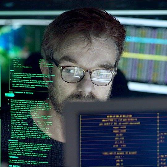 Man wearing glasses looking at various screens of comupter information