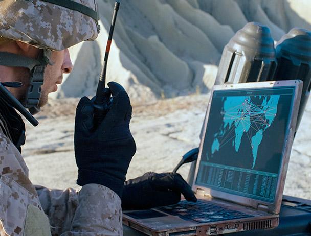 Soldier talking on a handheld 卫星 radio, looking at a map on a laptop