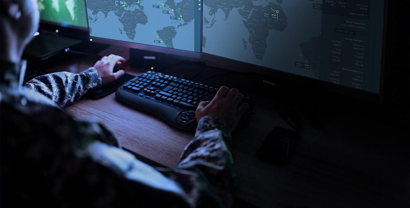一个穿着迷彩制服的人在电脑前工作的特写, 看着两个显示世界地图的显示器
