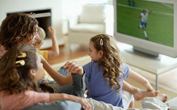 四口之家坐在沙发上看电视上的足球比赛