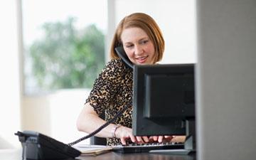 一个坐在电脑显示器后面的女商人, 在键盘上打字，打电话