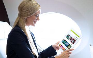 金发女商人坐在私人飞机上看平板电脑上的内容