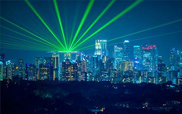 Image of a city skyline with bright green lights shining up into the night sky